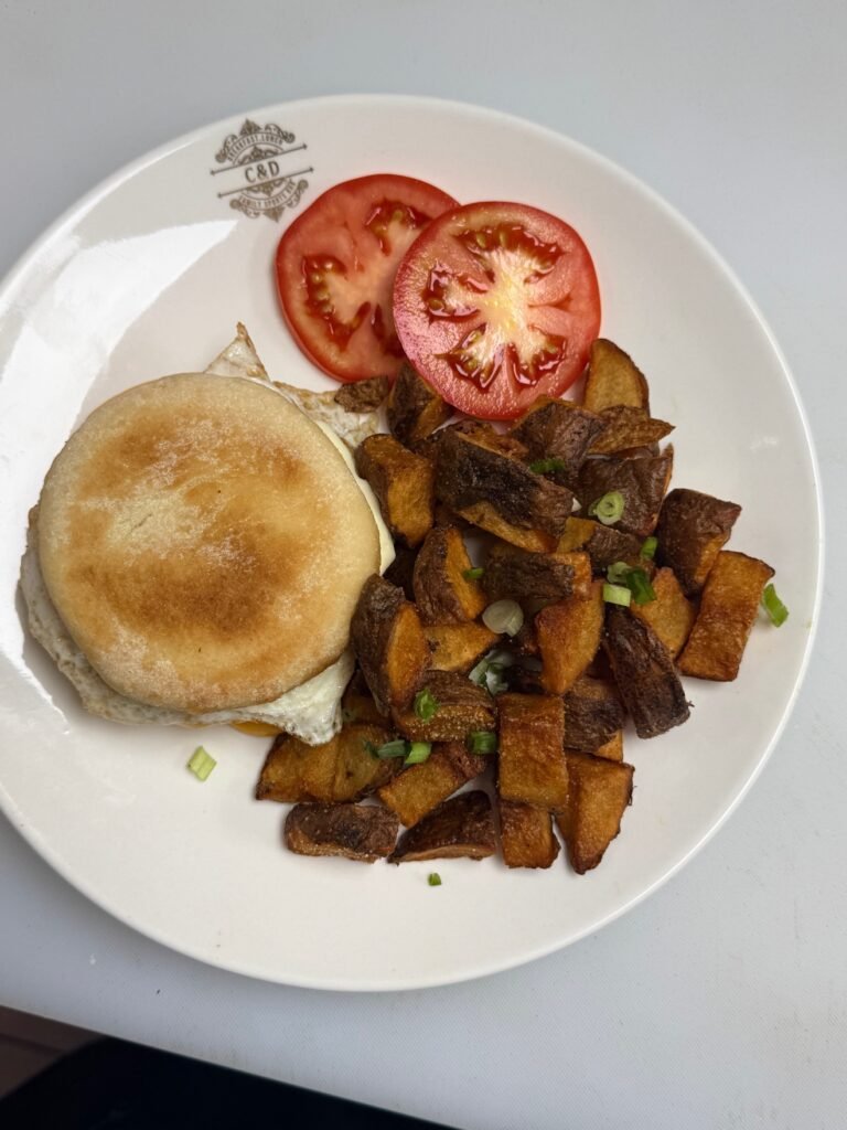 Breakfast egg sandwich on an English muffin with home fries and tomato at Cravings and Delight, a breakfast restaurant near Cavanagh Edmonton