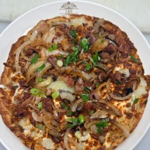 Perogy pizza topped with bacon, sauteed onions, and green onions on a C&D plate (full shot) at Cravings and Delight